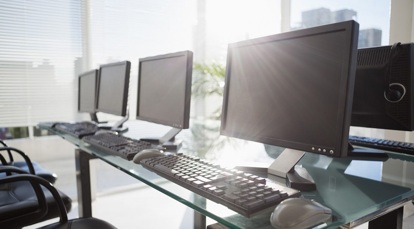 Row of office computers and keyboards on a glass desk, representing equipment moving in NYC.