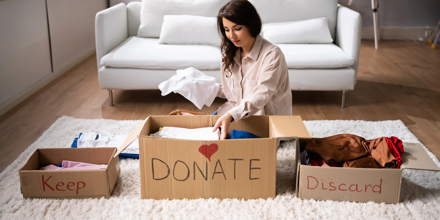 Woman sorting clothes into keep, donate, and discard boxes for spring cleaning and decluttering in NYC.