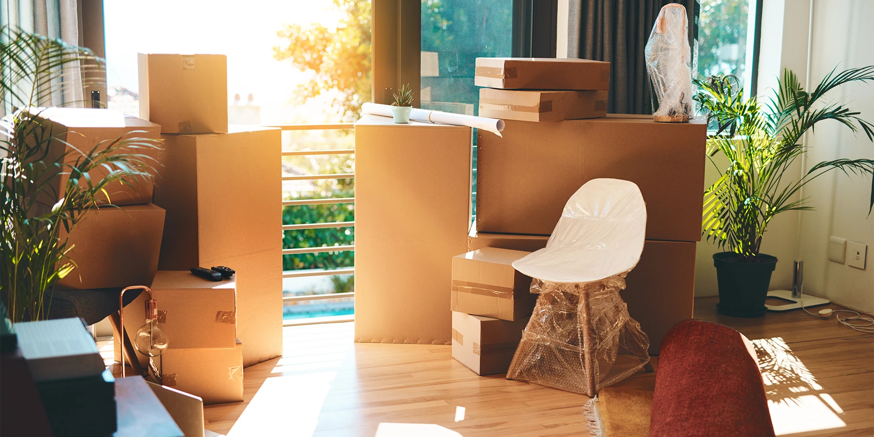 Stacked moving boxes and wrapped furniture in a sunlit apartment, representing moving with kids in NYC.